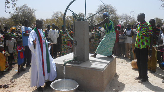 Der neue Brunnen wird geweiht, eine afrikanische Frau dreht das Wasserrad.